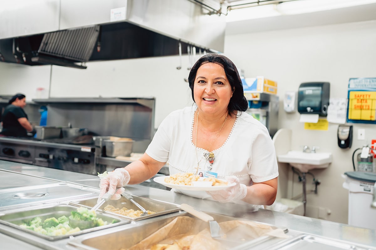 Woman in kitchen serving brocoli on to a plate.