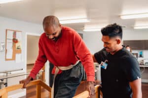 Physical therapist with his hand on man's back as he walks over rehab bridge in the rehab gym.